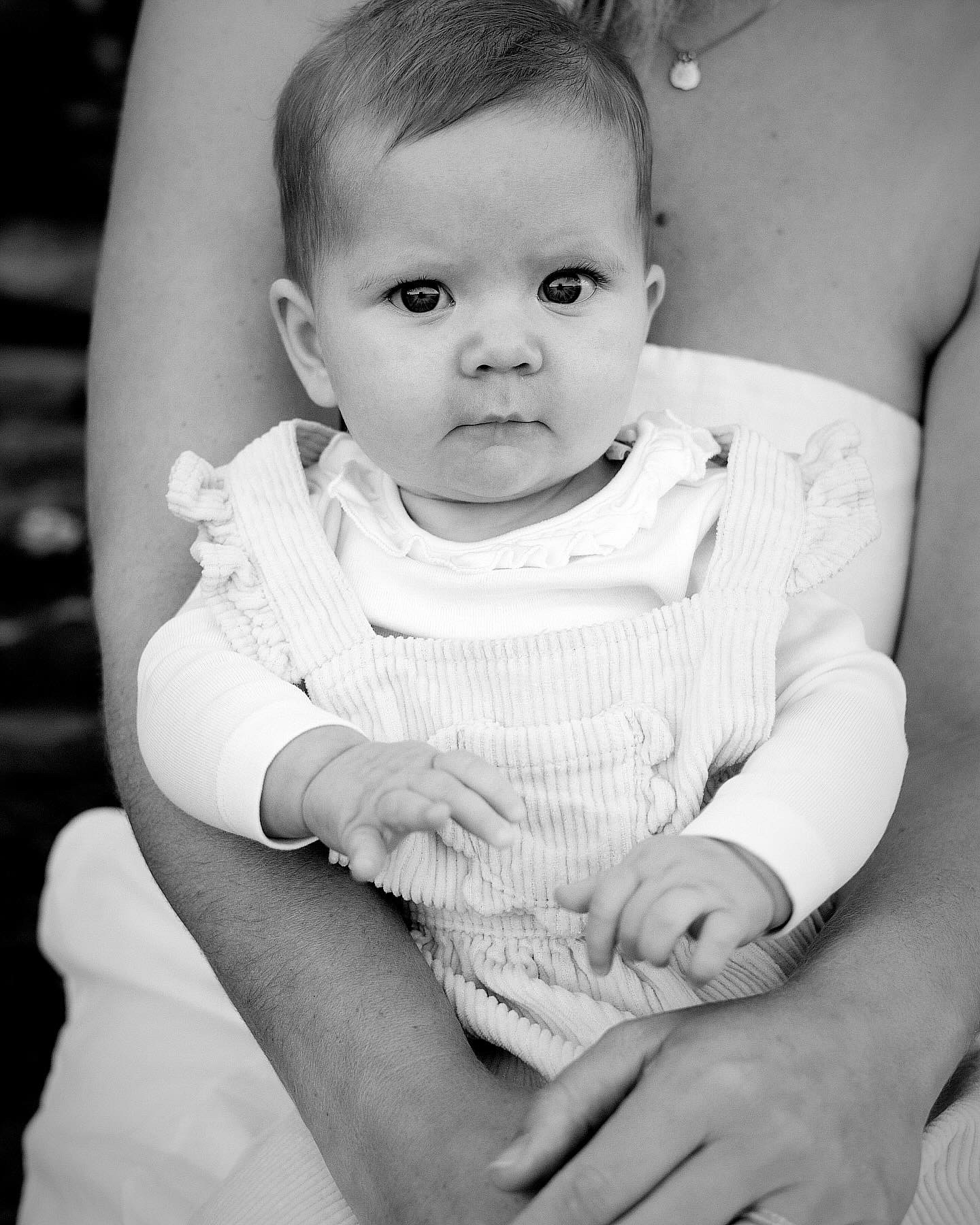 Baby in a knitted romper held in parent's arms, representing gentle postnatal home visit support